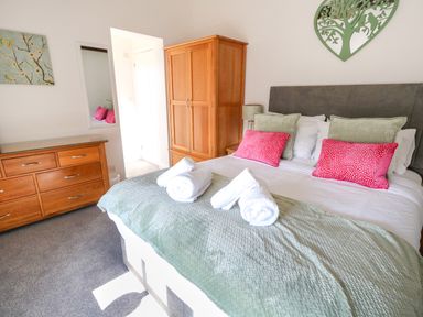 A bedroom with a bed with rolled towels and red pillows a wooden wardrobe and dresser with a wall mirror at Splash in Weymouth
