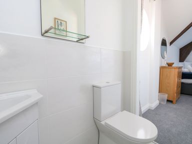 A bathroom with a toilet sink mirror and a view into a bedroom with a dresser and a bed at Splash in Weymouth