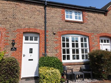 The exterior of a brick house with a white door numbered 7 and white-framed windows with bushes and two black chairs and a table outside at Splash in Weymouth