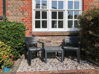 Two black chairs with a small table between them on a gravel area outside a brick house with white windows at Splash Weymouth