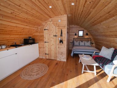 An interior of a wooden pod with a kitchenette a bed a small sofa and a coffee table at Glamping Pod 2 Presence in Lebberston