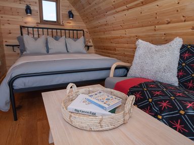 A bedroom with a bed a small table with a basket containing books and a chair with a cushion at Glamping Pod 2 Presence in Lebberston