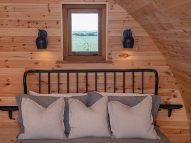 A bed with gray and white pillows under a small window with wooden walls and two black wall lamps at Glamping Pod 2 Presence in Lebberston