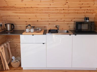 A kitchen counter with a kettle French press mugs a microwave sink and wooden walls at Glamping Pod 2 Presence in Lebberston