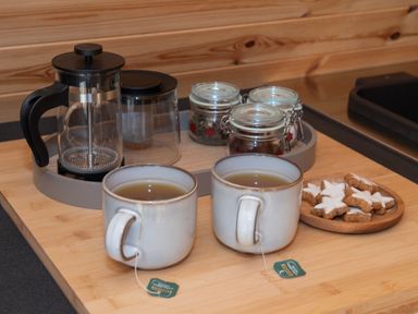Two cups of tea with tea bags on a wooden tray with a french press jars and star shaped cookies at Glamping Pod 2 Presence in Lebberston