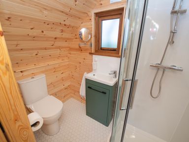 A bathroom with a toilet a green sink cabinet a shower and wooden walls at Glamping Pod 2 Presence in Lebberston