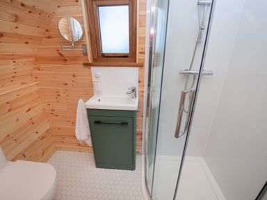A bathroom with a shower, small sink with green cabinet, toilet, wooden walls, and a small window at Glamping Pod 2 Presence in Lebberston