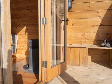 An open wooden door leading to a wooden interior with a chair and a stove at Glamping Pod 2 Presence Lebberston