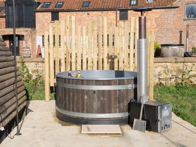 An outdoor wooden hot tub with drinks on the edge and a metal heater beside it at Glamping Pod 3 Harmony Lebberston
