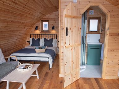 A wooden cabin interior with a bed sofa table and bathroom at Glamping Pod 3 Harmony Lebberston
