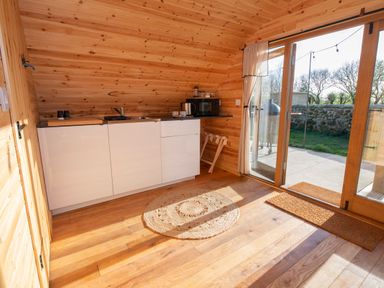 A kitchenette with white cabinets a sink a microwave and a window door leading outside at Glamping Pod 3 Harmony in Lebberston