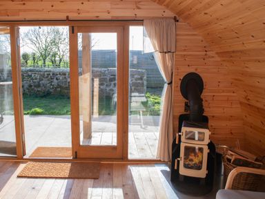 A room with wooden walls and floor a wood burning stove lit with fire and glass sliding doors leading outside at Glamping Pod 3 Harmony Lebberston