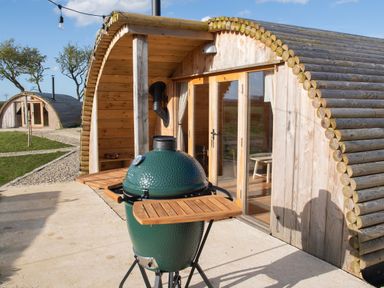 A wooden glamping pod with glass doors and a green ceramic barbecue grill outside at Glamping Pod 3 Harmony in Lebberston