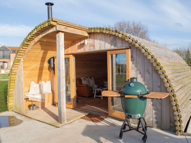 A wooden glamping pod with glass doors open showing a leather sofa inside and a green barbecue outside at Glamping Pod 4 Truce in Lebberston