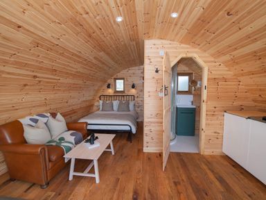 A wooden pod interior with a bed sofa coffee table and an open door to a bathroom at Glamping Pod 4 Truce in Lebberston