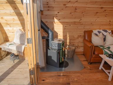A wood-paneled room with a wood stove basket of firewood leather sofa and a porch with bench and boots at Glamping Pod 4 Truce Lebberston