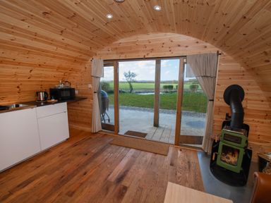 An interior with wooden walls and ceiling a small kitchenette stove and sliding glass doors looking out to a grass field at Glamping Pod 4 Truce in Lebberston
