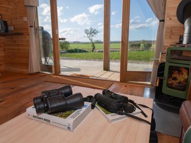 A wooden room with binoculars on books on a table and a glass door showing a field outside at Glamping Pod 4 Truce Lebberston