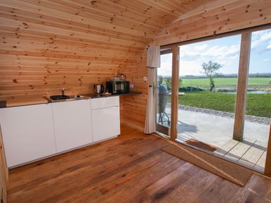 A wooden kitchen with white cabinets and a glass door opening to a green field at Glamping Pod 4 Truce in Lebberston