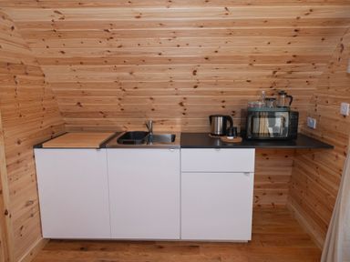 A small kitchen area with white cabinets a sink a microwave kettle and wooden walls at Glamping Pod 4 Truce Lebberston