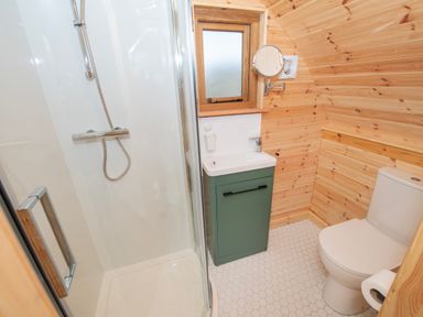 A bathroom with a shower, sink with green cabinet, toilet, and wooden paneled walls at Glamping Pod 4 Truce in Lebberston