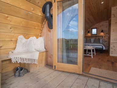 An open wooden door leading to a bedroom with a bed pillows and a wooden table with baskets inside a wooden cabin at Glamping Pod 4 Truce in Lebberston