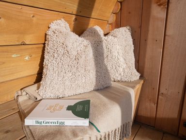 A wooden bench with two white textured pillows a beige blanket and a book titled Big Green Egg at Glamping Pod 4 Truce Lebberston