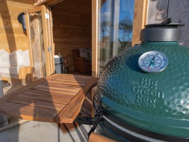 A green outdoor grill with wooden side table and interior wooden room with chair at Glamping Pod 4 Truce in Lebberston