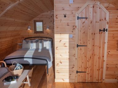 A wooden bedroom with a bed a small window a wooden door and a table with a basket and binoculars at Glamping Pod 5 Shelter in Lebberston