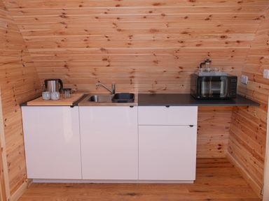 A kitchen area with a sink microwave kettle cups and wooden walls at Glamping Pod 5 Shelter Lebberston