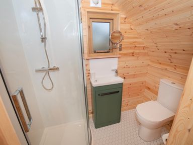 A bathroom with a shower, toilet, sink with green cabinet, and small window at Glamping Pod 5 Shelter Lebberston