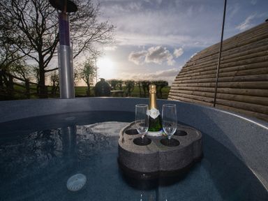 A hot tub with a floating tray holding a bottle and two glasses outside near a wooden structure at Glamping Pod 5 Shelter in Lebberston