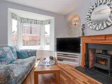 A living room with a floral sofa, wooden coffee table with a board game, TV on a white stand, and a fireplace at Metcalfe House in Compton Dundon