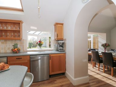 A kitchen with wooden cabinets and a dishwasher next to an arched doorway leading to a dining room at Metcalfe House Compton Dundon