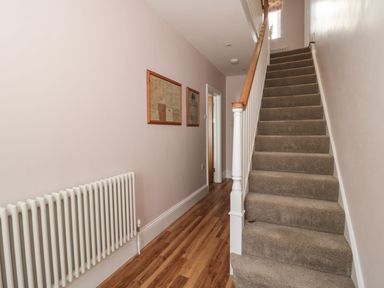 A hallway with wooden floor carpeted stairs radiator and framed pictures on the wall at Metcalfe House in Compton Dundon