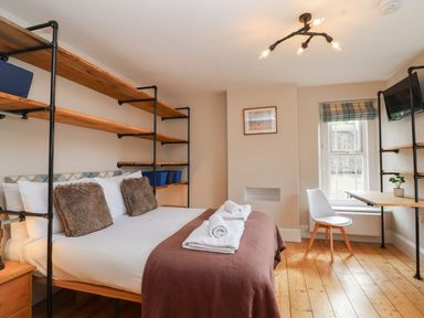 A bedroom with a bed with rolled towels pillows and shelving a desk with a chair and a window at Metcalfe House in Compton Dundon