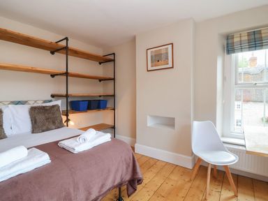 A bedroom with bed white chair wooden shelves and window at Metcalfe House in Compton Dundon