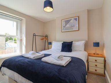 A bedroom with a bed with white and blue bedding two rolled towels a window side tables with lamps and a clothes rack at Metcalfe House in Compton Dundon
