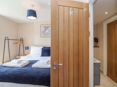 A bedroom with a double bed covered with blue and white linens two rolled towels on the bed a wooden door partly open a clothes rack with hangers a bedside table with a lamp and bedside radio a framed artwork on the wall at Metcalfe House in Compton Dundon