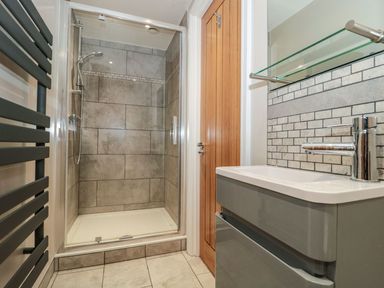 A bathroom with a tiled shower cabin a grey sink unit and a wooden door at Metcalfe House in Compton Dundon
