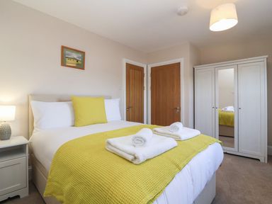 A bedroom with a bed with yellow bedding two wooden doors a white wardrobe with a mirror and a bedside table with a lamp at Metcalfe House in Compton Dundon