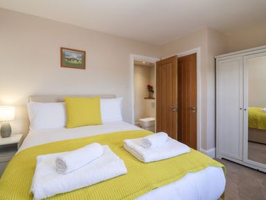 A bedroom with a double bed yellow bedding and rolled towels a lamp a wooden door and a white wardrobe with mirror at Metcalfe House in Compton Dundon