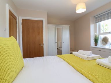 A bedroom with a bed with yellow bedding a white wardrobe with mirrors a wooden door and a window with a small mirror and a plant on the sill at Metcalfe House in Compton Dundon