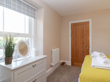 A bedroom with a white dresser with a round mirror and plant near a window a yellow bedspread on a bed and a wooden door at Metcalfe House in Compton Dundon