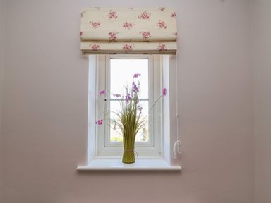 A window with floral Roman blinds and a vase with tall grass and purple flowers on the sill at Metcalfe House in Compton Dundon