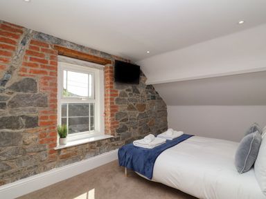 A bedroom with a bed towels and pillows stone and brick wall a window with a plant and a wall mounted tv at Metcalfe House in Compton Dundon