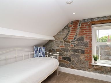 A bedroom with a white metal bed frame a blue patterned pillow a window and a stone and brick wall at Metcalfe House in Compton Dundon