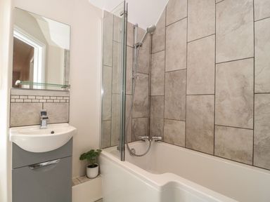 A bathroom with a bathtub shower combination a sink with a mirror and a small potted plant at Metcalfe House in Compton Dundon