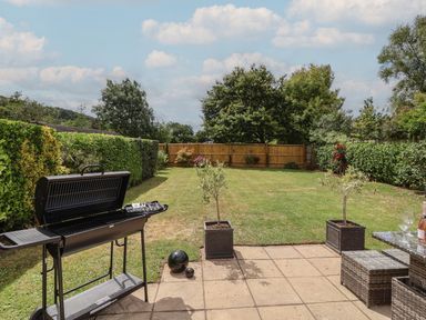 A backyard with a barbecue grill on a patio and a grass lawn with trees and shrubs at Metcalfe House in Compton Dundon