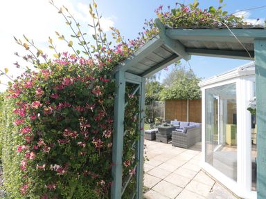 A garden patio with wicker furniture and a blue wooden arch covered in flowering vines at Metcalfe House in Compton Dundon